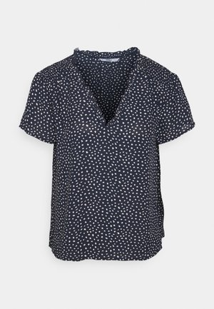 Blouse bleu marine à manches courtes avec de petites formes géométriques blanches dispersées, encolure en V et léger détail de volants au col.