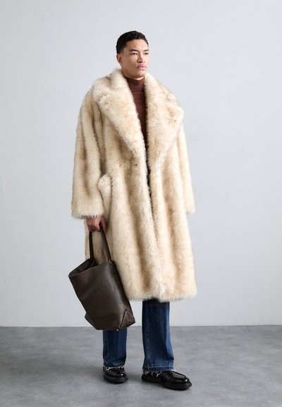 Šviesiai rudas dirbtinės kailio paltas su plačiais apykaklės kraštais, šoninėmis kišenėmis ir minkšta tekstūra. Sutampa su tamsiomis džinsomis, juodais batais ir rudomis odinėmis rankinėmis.