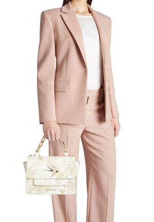 Donna che indossa un completo rosa chiaro che tiene una borsa bianca con motivo, manici a catena dorata e decorazione a forma di uccello.