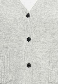 Sivi pleteni kardigan s V-izrezom, pet crnih gumba, rebrastim džepovima i mekom teksturom.