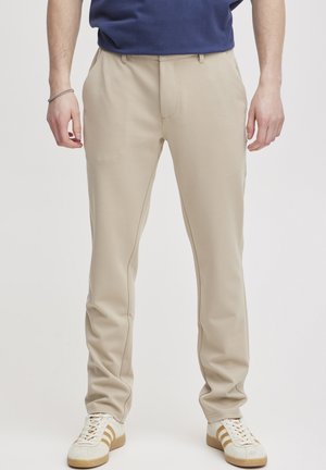 Beige tailored pants made of stretchy material, featuring a smooth texture, straight cut, and subtle side seam detailing.