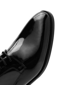 Chaussure de ville en cuir verni noir avec un bout pointu, équipée d'un système de laçage, finition lisse et brillante, et couture discrète le long du bord.