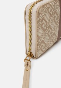 Portafogli con zip di colore beige con un motivo intrecciato e accenti lisci. L'hardware dorato, una tracolla laterale e una finitura testurizzata arricchiscono il suo design.