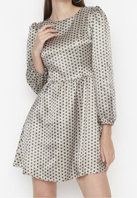 Femme portant une robe à manches longues, longueur genou, avec des épaules bouffantes et un motif à carreaux noir et blanc.