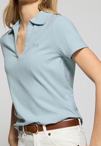 Light blue polo shirt with a v-neck and short sleeves. Made of smooth fabric, features a small "POLO CLUB" logo on the chest.