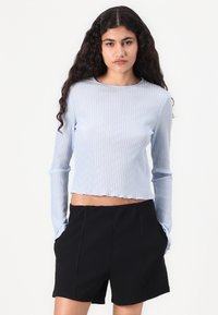 Lyseblå ribbet langermet topp med en kortet hem, kombinert med svarte høyhårede shorts som har sidelommer og en skreddersydd snitt.