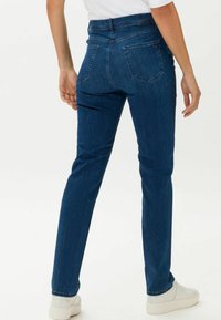 Dunkelblaue Denim-Jeans mit geradem Schnitt, Gesäßtaschen und hohem Bund. Getragen mit weißen Sneakers.