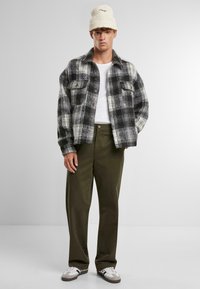 Rutete, oversized flanelljakke i svart og hvitt, med knapper foran og to brystlommer. Kombinert med olivengrønne bukser og hvite joggesko.