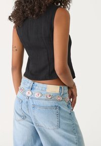 Czarny bezrękawnik zestawiony z jasno-niebieskimi dżinsami z wysokim stanem. Dżinsy mają metalowy pasek z kwiatowymi akcentami w srebrnym i różowym kolorze.