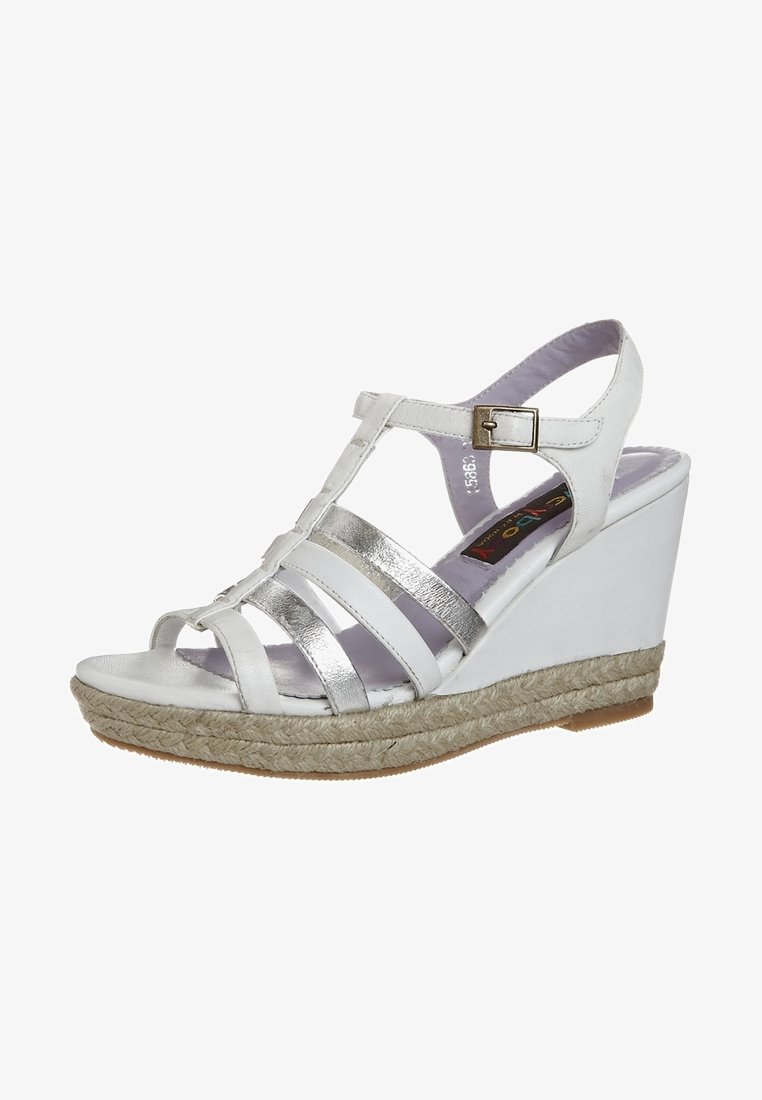Sandale wedge blanche avec des brides croisées métalliques argentées, une boucle réglable et une plateforme de style espadrille texturée.