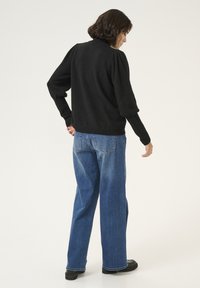 Pull-over noir avec des épaules structurées, associé à un jean bleu clair à jambes larges et des chaussures noires ; texture lisse, coupe décontractée.