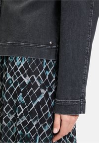 Czarna kurtka dżinsowa o skróconym kroju z detalami w srebrnym kolorze. W połączeniu z wzorzastym ubraniem, które ma turkusowe i czarne romby.