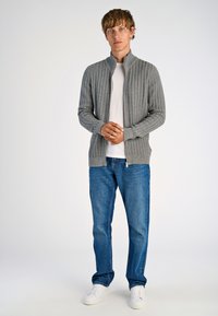 Gray zip-up cardigan with a textured pattern, worn over a white T-shirt, paired with blue jeans and white sneakers.