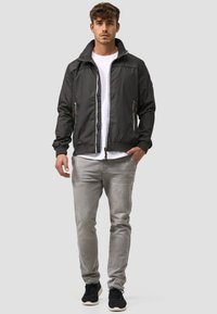 Dark gray zip-up jacket with high collar, two front pockets, and contrasting white zippers, paired with light gray pants and black sneakers.