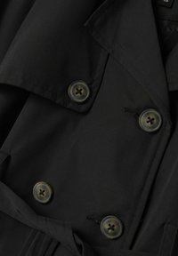 Čierny trench coat s klopami, ktorý má veľké zaoblené gombíky so štyrmi otvormi a hladký textúru látky.