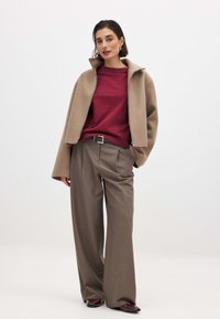 Béžová skrátená bunda, vínový sveter a voľné hnedé nohavice. Hladké textúry, uvoľnený strih a jednoduchý detail opasku s špicatými topánkami.