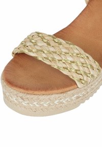 Sandalo espadrille con una fascia intrecciata beige con accenti dorati, soletta in pelle color cuoio e piattaforma in juta testurizzata con finitura intrecciata.
