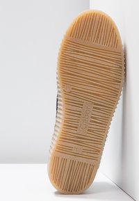 Semelle de chaussure en caoutchouc texturé avec des rainures horizontales et verticales, un logo circulaire, et le nom de la marque "Gabor" embossé.