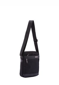 Borsa a tracolla nera realizzata in tessuto resistente con una base in pelle liscia, dotata di una tasca frontale con zip e cinturino regolabile.