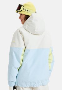 Lightweight ski jacket with a color-block design featuring white, light blue, and pastel green. Includes a hood and elastic cuffs.