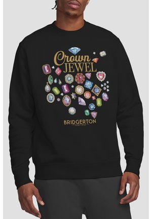 Man wearing black sweatshirt with colorful jewel illustrations, gold text "Crown Jewel," and "Bridgerton" at bottom.