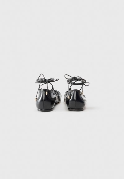 Black leather ballet flats with decorative stitching, ribbon ties at the ankle, and gold-tone hardware accents at the back.