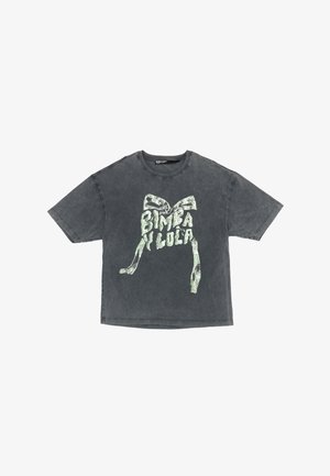 Camiseta gris de gran tamaño hecha de algodón suave, con una gran impresión gráfica verde de un lazo y el texto "Bimba y Lola" en el frente.