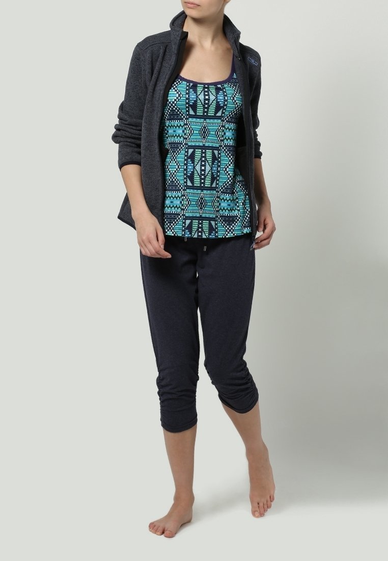 Giacca in pile con zip di colore grigio scuro, canottiera stampata in turchese, blu navy e nero, abbinata a pantaloni jogger scuri, indossati a piedi nudi.