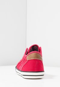 Baskets décontractées rouges avec semelle blanche et rayures noires, patch marron au talon, et doublure intérieure à carreaux, photographiées de dos sur fond blanc.