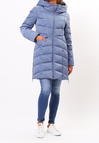 Puffjacka i ljusblått, quiltad design med huva, dragkedjestängning och sidofickor. Matchat med slim jeans och vita sneakers.