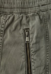 Zbliżenie na szarą elastyczną talię i pionowy metalowy zamek błyskawiczny na spodniach z tkaniny z widocznymi detalami szwów.