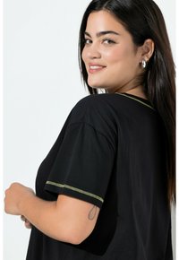 Camiseta negra de manga corta, con costuras de acento verdes a lo largo del cuello y los puños. Textura suave y corte relajado.