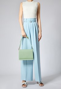 Borsa a tracolla in pelle verde chiaro con superficie testurizzata, accessori in argento e una maniglia superiore. Abbinata a una maglietta bianca a coste e pantaloni larghi blu pallido.