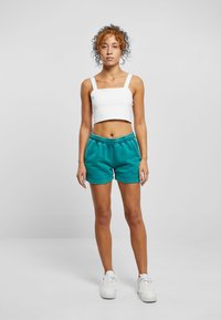 White cropped tank top with thick straps, paired with teal shorts featuring an elastic waistband. Model wearing white sneakers.