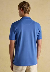 Modrá polo košile s krátkým rukávem z měkké tkaniny, s límečkem a bočními rozparky, s jemnou texturou a čistým švem na zadní straně.