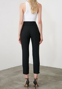 Černé elegantní kalhoty s vysokým pasem a zúženými nohavicemi, spolu s bílým topem bez rukávů. Materiál vypadá hladce a pružně.
