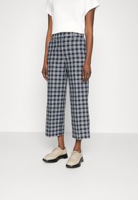 Höga marinblå rutiga byxor med kortade ben och vitt rutig mönster, tillsammans med beige snörskor. Slät tygstruktur.