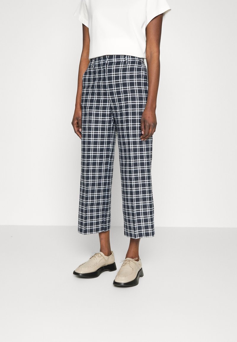 Höga marinblå rutiga byxor med kortade ben och vitt rutig mönster, tillsammans med beige snörskor. Slät tygstruktur.