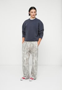 Navy crewneck sweatshirt, loose fit. Light gray pants with leafy pattern, drawstring waist. Red-and-white sneakers. Minimalist design.