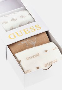 Tre paia di calze in una scatola. Un paio è beige, un altro è bianco con piccoli cuori marroni, e l'ultimo ha un motivo con un logo discreto.