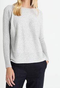 Hellgrauer, langärmeliger Pullover mit strukturiertem Körper und glatten Ärmeln; lockere Passform und runder Halsausschnitt, kombiniert mit dunklen Hosen.