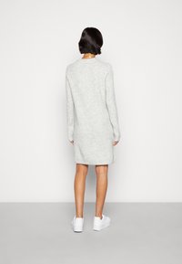 Abito in maglia grigio a maniche lunghe con vestibilità rilassata, caratterizzato da un collo rotondo e una texture sottile, abbinato a sneakers bianche.