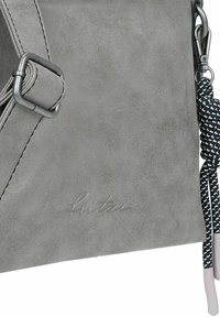 Bolso cruzado de ante gris con un hebilla metálica y una correa trenzada, que presenta un sutil detalle de logotipo en relieve. Textura suave.