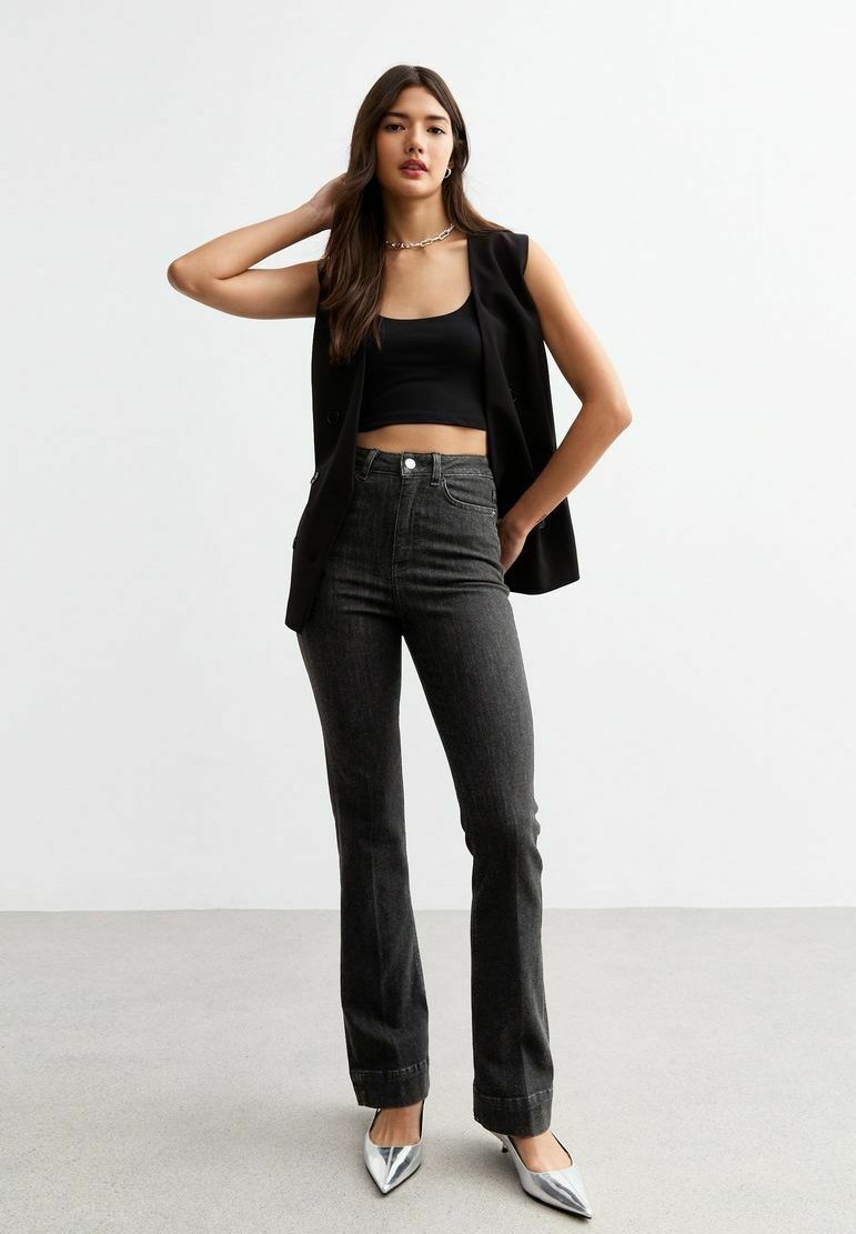 Blazer sans manches noir sur un crop top noir, associé à un jean en denim gris foncé taille haute et des escarpins argentés à bout pointu.