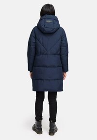 Marineblå pufferjakke med hætte, der har en quiltet design og skrå sømme. Sammen med sorte leggings og ankelstøvler.