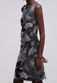 Ärmlös, knälång svart och vit klänning med abstrakta geometriska virvlar och prickmönster som bärs av en stående person.