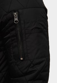 Czarna pikowana rękaw kurtki o teksturowanym wykończeniu, z kieszenią na zamek w kolorze srebrnym i płaską kieszenią powyżej.