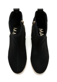 Botas de tobillo de ante negro con una silueta esbelta, detalles de cremallera dorada y una textura suave. Suela beige visible a lo largo del borde.