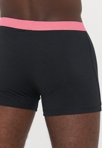 Schwarze Boxershorts aus glattem Stoff mit einem lebhaften pinken elastischen Bund und einer engen Passform. Nahtdetails sind an den Seiten sichtbar.
