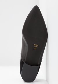 Svart läder- och mockahögklackad sko med spetsig tå, slät yta och gummisula. Märkt "Made in Spain" och storlek 37 på undersidan.